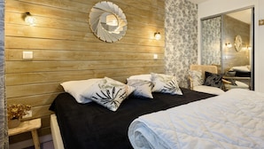 Un dormitorio con pared de madera, un espejo redondo, una cama con cubrecama negro y almohadas estampadas, una mesita de noche con una planta y un espejo grande en la pared.