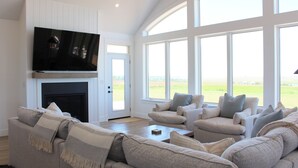 Ein Wohnzimmer mit Kamin, einem darüber angebrachten Fernseher und einem großen Fenster mit Blick ins Freie.