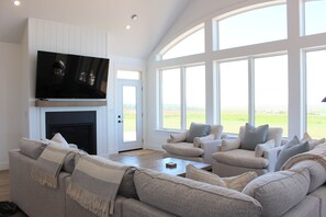 Ein Wohnzimmer mit Kamin, einem darüber angebrachten Fernseher und einem großen Fenster mit Blick ins Freie.