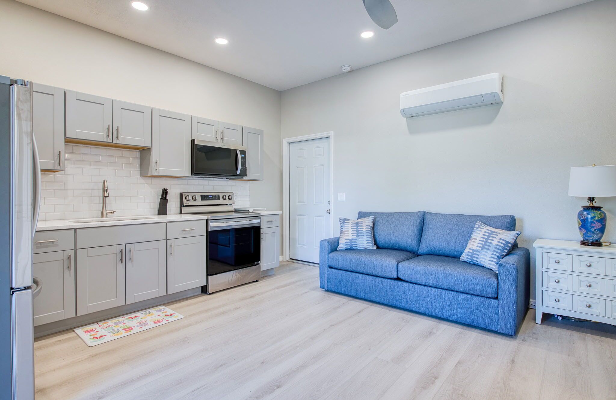 A modern kitchen with white cabinets, a microwave, oven, and a blue sofa in a living area.