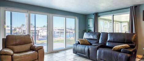 A living room with a brown leather sofa, a brown leather armchair, and a large sliding glass door leading to a patio.