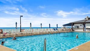 En swimmingpool med en livräddarstation, solstolar och en byggnad med en skylt där det står ”HÄMTAS HÄR”.