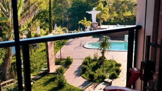 A pool area with a statue, surrounded by greenery and a paved walkway. - Pousada Finca dos Anjos (Passa Quatro)