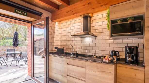A modern kitchen with a brick backsplash, wooden cabinets, a stainless steel range hood, and a built-in microwave.