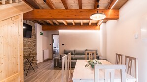 A wooden interior with a dining table and chairs, a stone wall, and a sofa in the background.