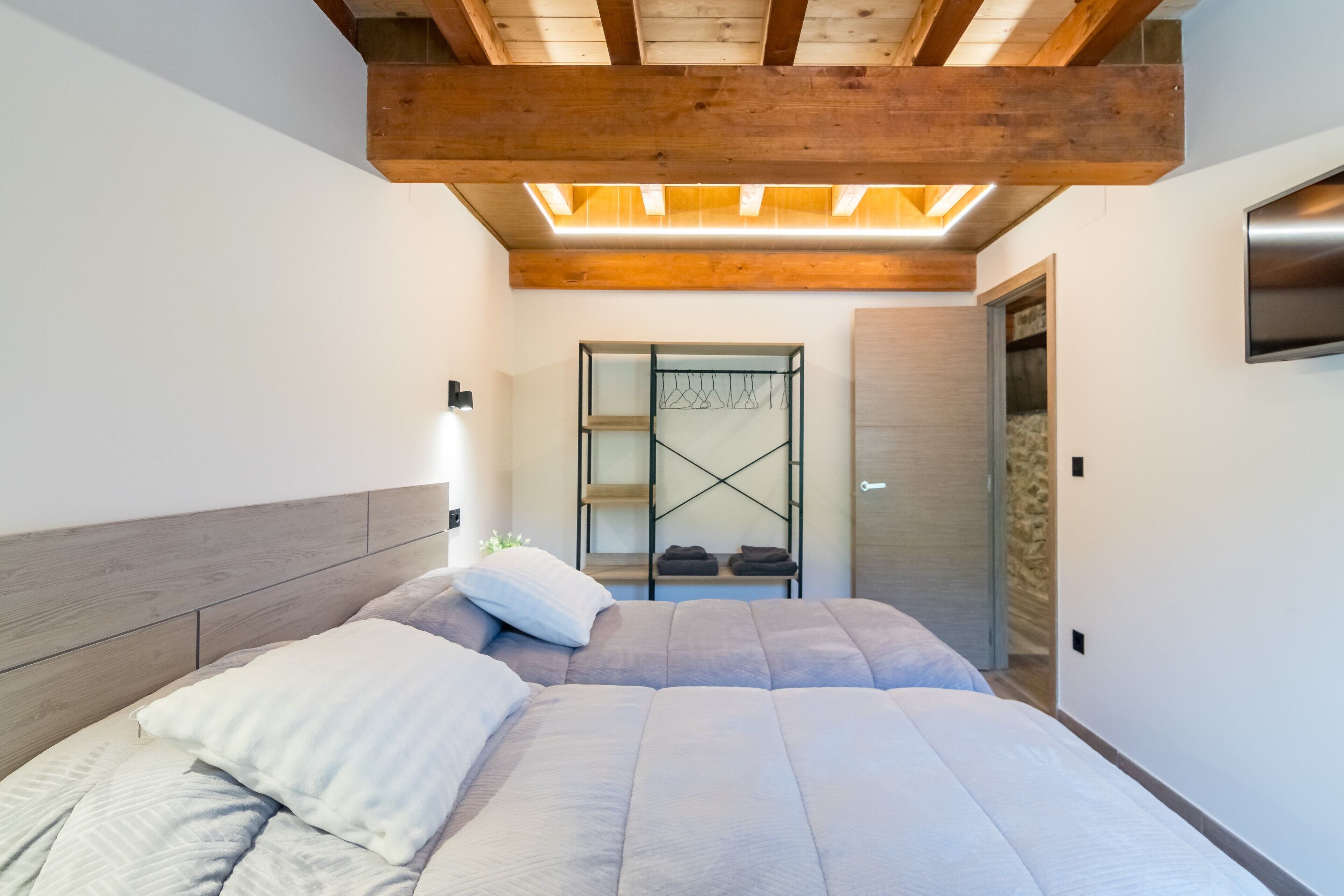 Un dormitorio con techo de madera, una cama con cabecera, un armario empotrado y un televisor fijado a la pared.
