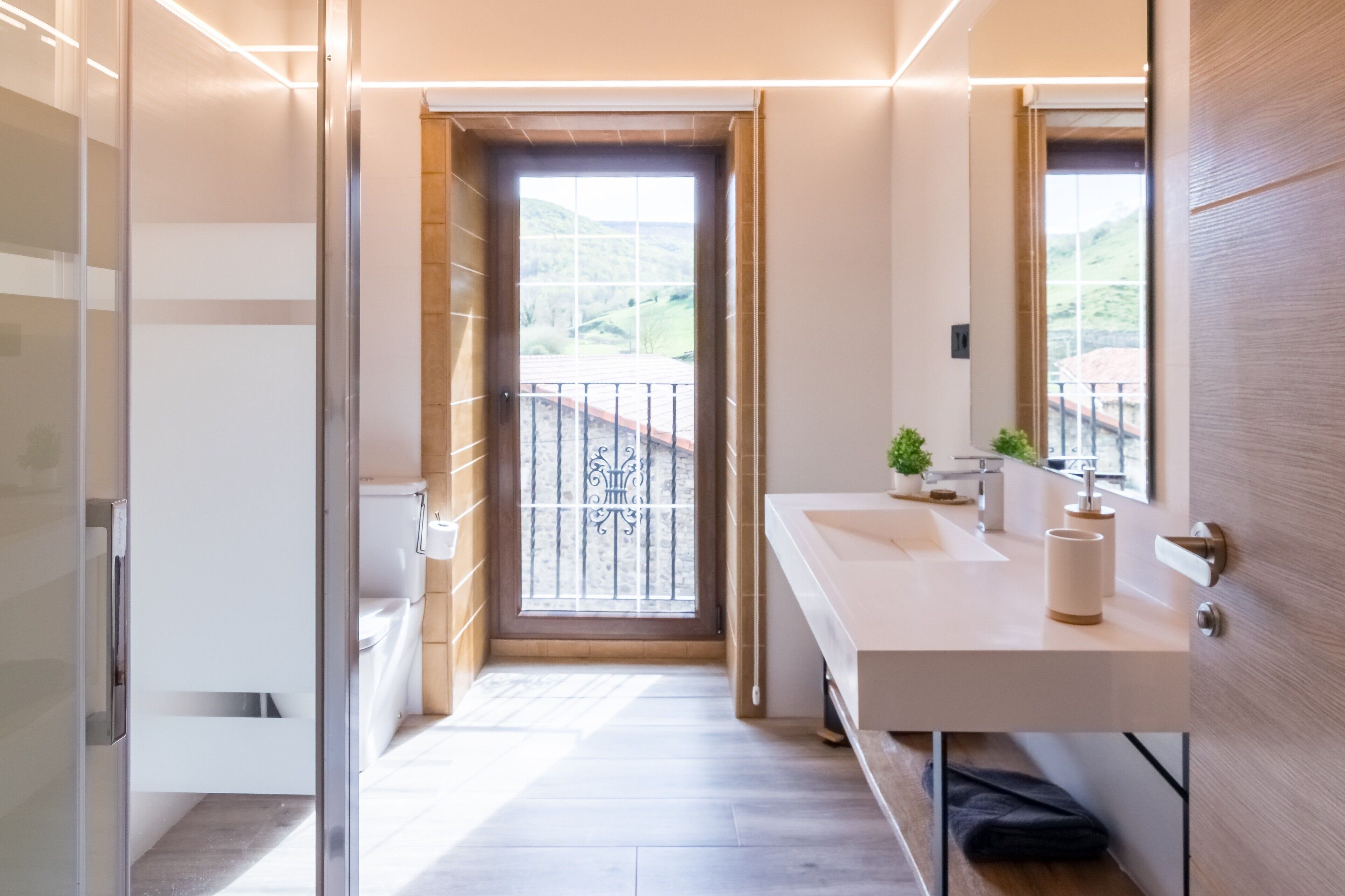Ein modernes Badezimmer mit einem großen Spiegel, einem weißen Waschbecken und Blick auf einen Balkon.
