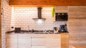 A kitchen with white tiled walls, a wooden ceiling, and a central island with a black range hood.