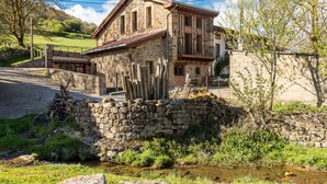 A stone building with a balcony, a stone wall, and a small stream.