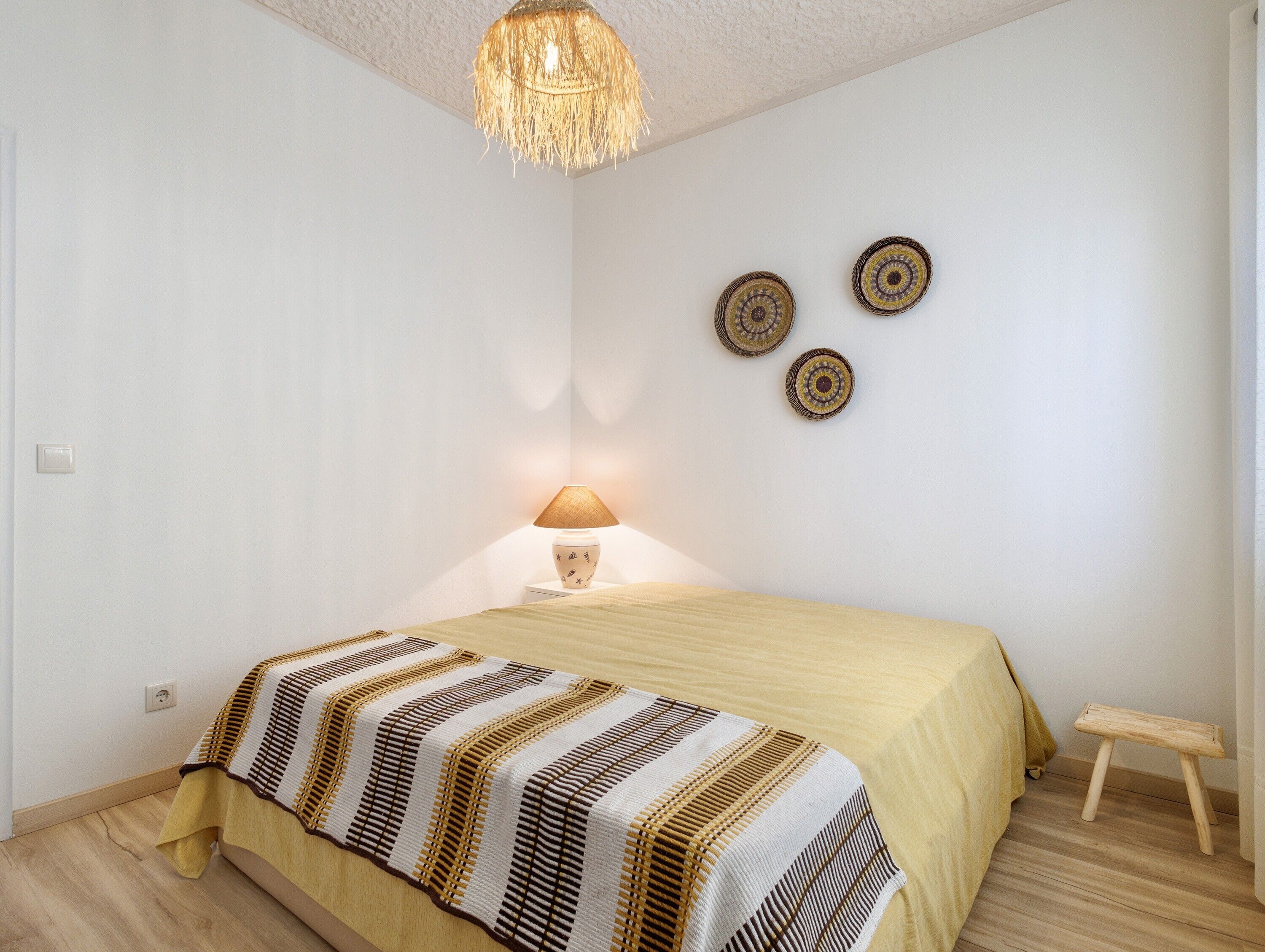 A bedroom with a bed, a bedside lamp, a small stool, and wall decor.