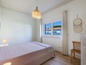 Une chambre à coucher avec un lit, un luminaire suspendu, une fenêtre avec des rideaux et un élément décoratif mural.