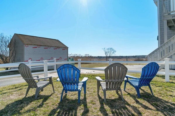 Three Adirondack chairs facing a building with a white fence and a clear sky. - Crescent Breeze at the Beach (Wells)
