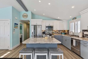A modern kitchen with a central island, stainless steel appliances, and light blue walls. - Crescent Breeze at the Beach (Wells)
