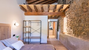 Quarto com teto de madeira, parede de pedra e cama com roupa de cama branca.