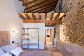 Una camera da letto con soffitto in legno, parete in pietra e un letto con biancheria bianca.