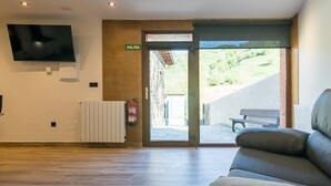 Um interior moderno com uma TV de tela plana, um sofá, um extintor de incêndio e uma porta com a inscrição 'SALIDA' que dá para o exterior.