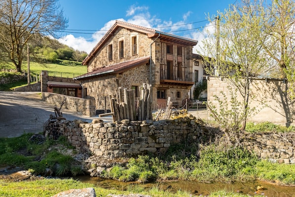 Un edificio in pietra con un balcone, un muro di pietra e un piccolo ruscello.