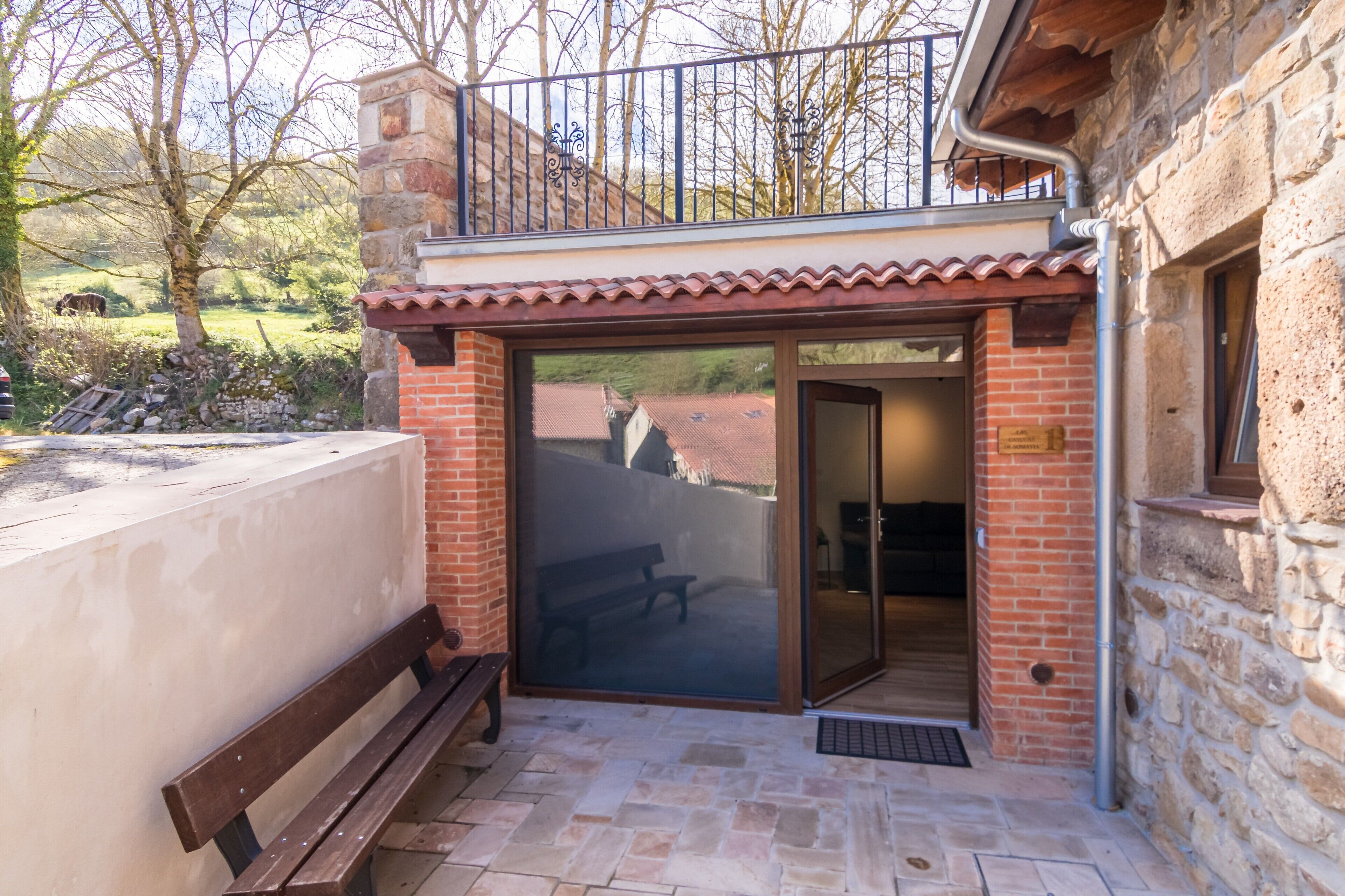 A patio with a bench, a stone wall, and a glass door leading to an interior space.