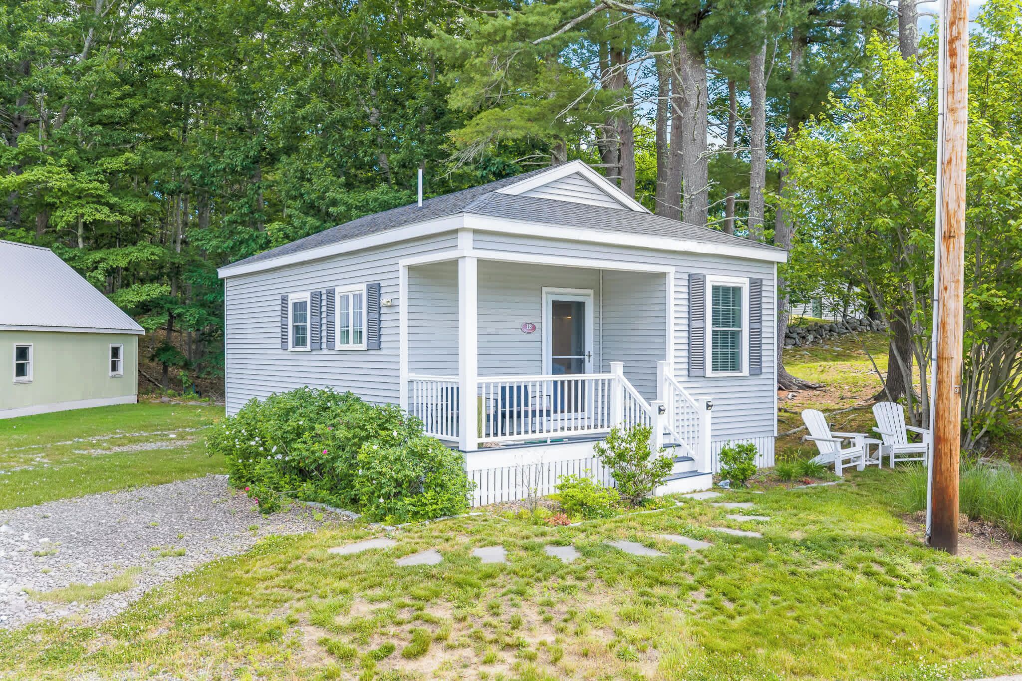 A small, single-story house with a porch, surrounded by a grassy yard and trees.