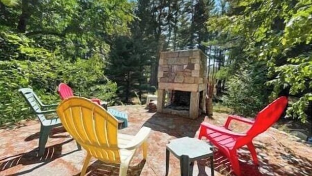 Une cheminée en pierre entourée de verdure, et un espace extérieur aménagé avec des chaises et des tables.