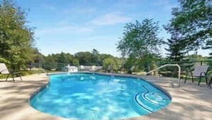 Une piscine rectangulaire à bord incurvé, entourée d’une terrasse en béton et de rampes métalliques.
