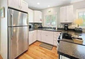 A modern kitchen with white cabinets, a stainless steel refrigerator, and a black countertop.