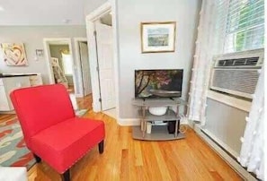 A living room with a red chair, a television on a stand, and a window with blinds.