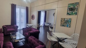 A living room with purple sofas, a glass coffee table, white chairs, and a dining table. - EVA LUXURY BASTIONE (Cagliari)