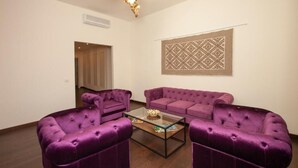 A living room with a purple sofa set, a glass coffee table, and a decorative wall hanging. - EVA LUXURY BASTIONE (Cagliari)