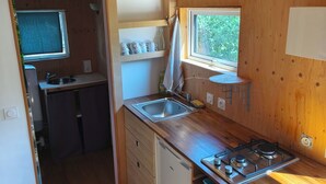 Een kleine keuken met houten kastjes, een inbouwfornuis, een spoelbak en een raam voor natuurlijk licht.