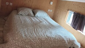 Een slaapkamer met een groot bed, houten wanden, een raam met gordijnen en wandlampen.
