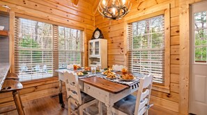 Un interior de madera con una mesa de comedor lista para una comida, rodeada de ventanas con persianas.