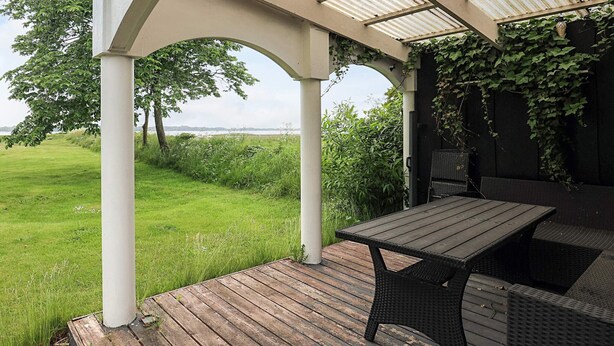 Een overdekt terras buiten met een tafel en stoelen, een uitzicht op het landschap en een pergola.