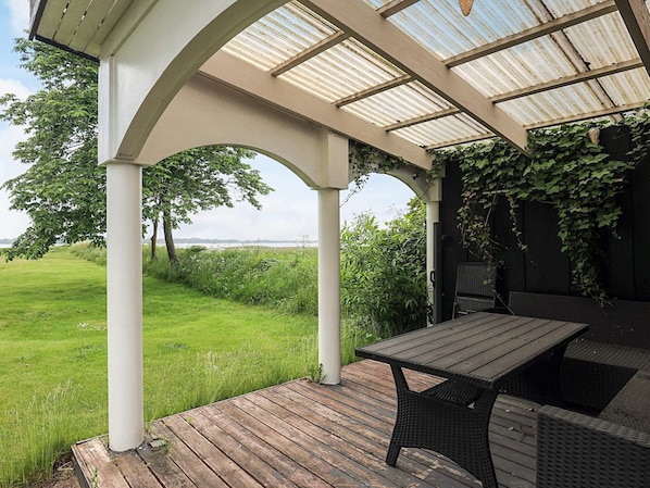 A covered outdoor patio with a table and chairs, a view of the landscape, and a pergola structure. - 4 Star Holiday Home in Roslev (Roslev)