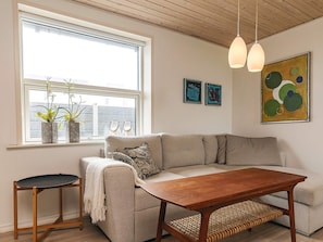 A modern living room with a sofa, a coffee table, a small side table, and a window with plants. - 4 Star Holiday Home in Roslev (Roslev)