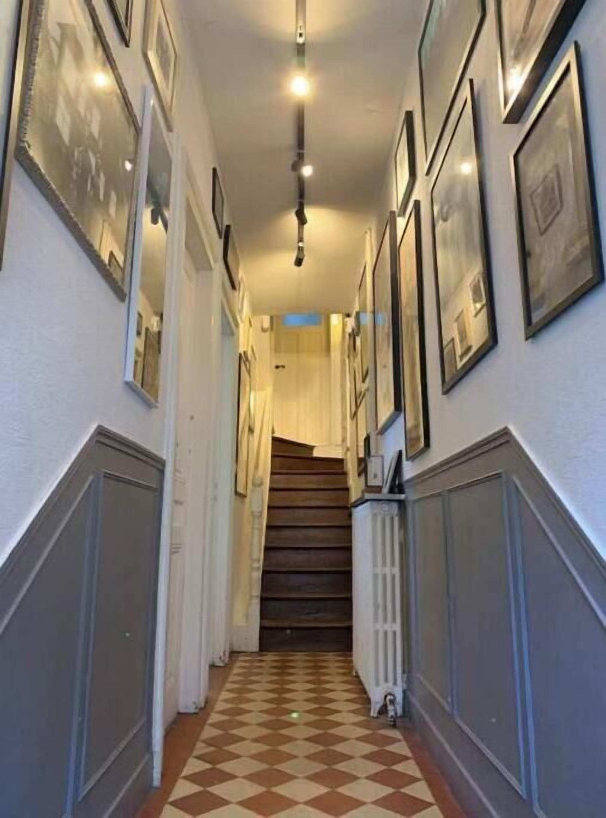 A hallway with a checkered floor, framed pictures on the walls, and a radiator on the right.