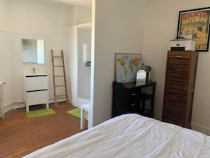 A bedroom with a bed, a dresser, a desk with a map, a ladder, and a wardrobe.