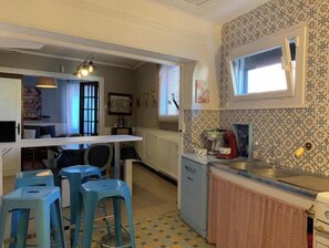 A compact kitchen with a dining area, a small refrigerator, and a window with blinds.