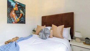 A bedroom with a brown upholstered headboard, a white bedspread, and a blue knitted blanket. - Una Estancia Moderna y Confortable (Puerto Plata)