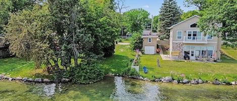 A residential area with a pond, a large tree, and a two-story house with a patio.