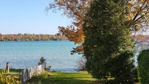 Blick auf einen See mit einer Holzlattenzaun, einer Rasenfläche und einem Baum.