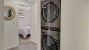 Ein Waschraum mit zwei großen Waschmaschinen mit Frontlader, einem Spiegel und einem Bett im angrenzenden Zimmer.