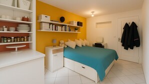 A bedroom with a bed, bedside tables, a shelf with books and containers, a desk, and a door with coats hanging. - Sudette 5 min from Paris with garden (Ivry-sur-Seine)