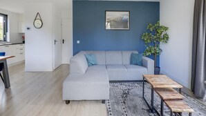 Uma sala de estar moderna com um sofá cinza, uma mesa de centro de madeira, uma parede azul e uma janela.
