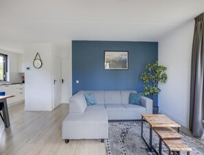 Ein modernes Wohnzimmer mit einem grauen Sofa, einem Holztisch, einer blauen Wand und einem Fenster.