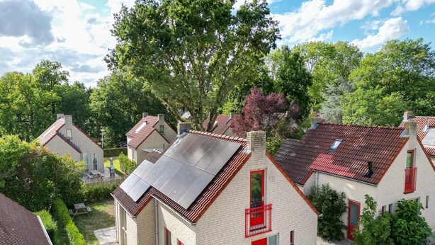 Bairro residencial com casas com portas vermelhas, painéis solares e um jardim bem cuidado.