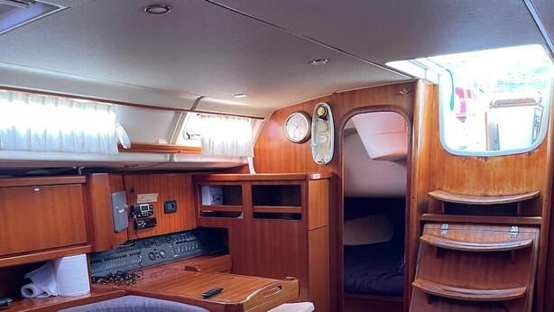 Interior compacto e bem iluminado, com mesa de madeira, assentos acolchoados, painel de controle e uma pequena janela.