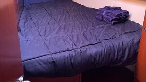 Um quarto compacto com uma cama de solteiro, cabeceira de madeira e um pequeno espaço para sentar.