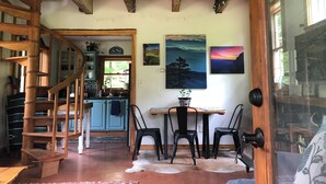 A rustic interior with a wooden staircase, a dining area with chairs, a kitchen with blue cabinets, and artwork on the walls. - Oasis in the Blue Ridge Rt. 151 Brew Ridge Trail-Cozy Cottage in the mountains (Afton)