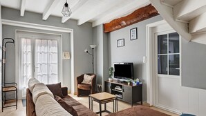 Ein Wohnzimmer mit einer Couch, einem Fernseher, einem Sessel und einem kleinen Tisch.
